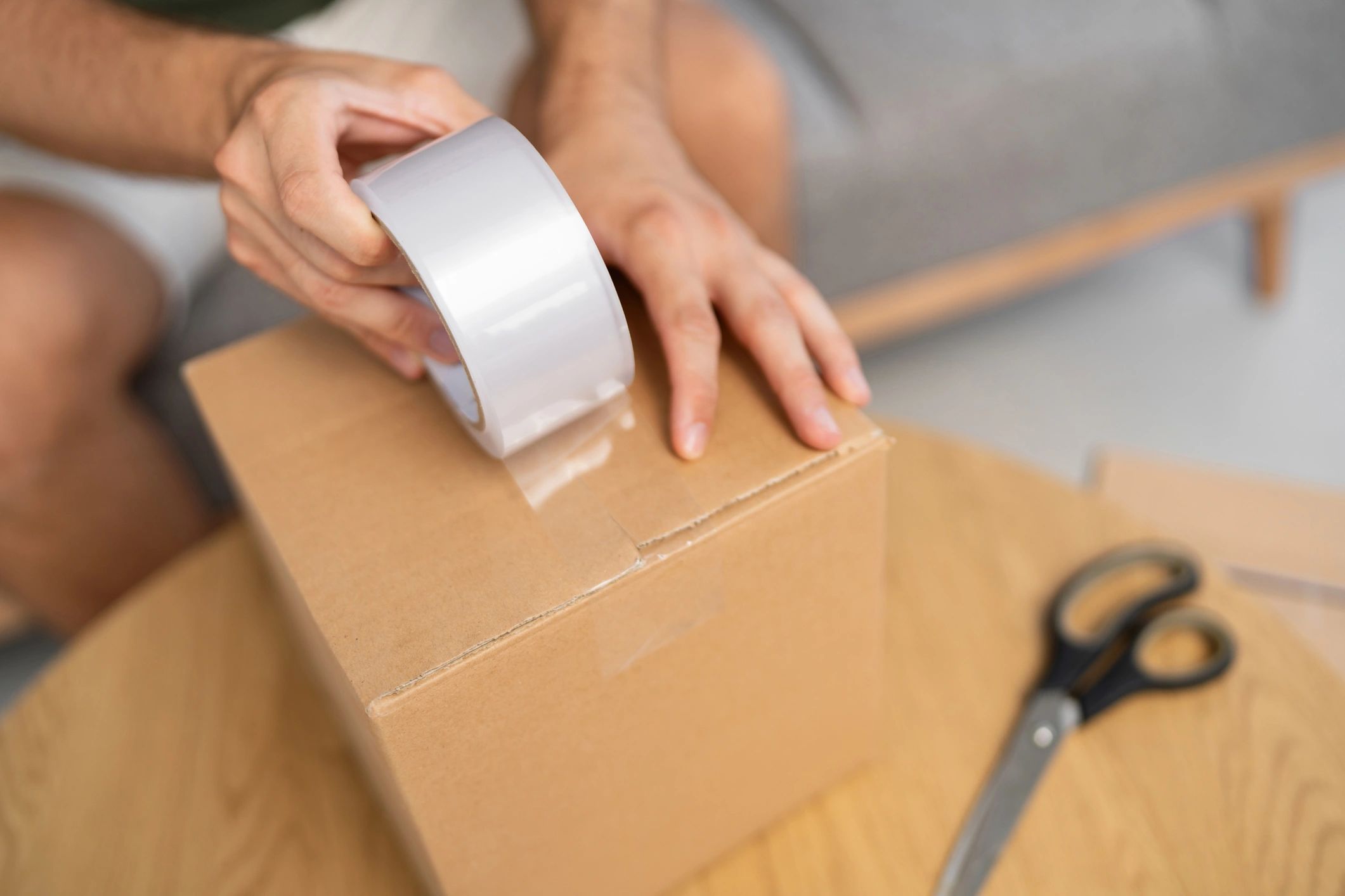 Hands sealing a small cardboard box with packing tape